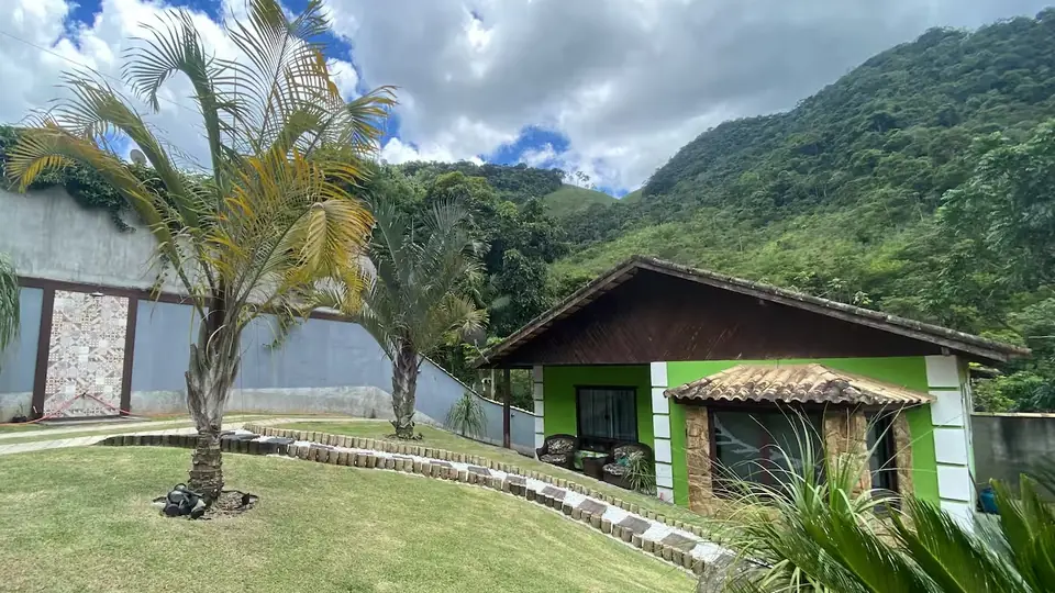 Fachada da casa verde, com o gramado na frente e o morro atrás