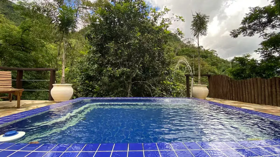 Piscina de ladrilho azul com o morro de mata atlântica ao fundo