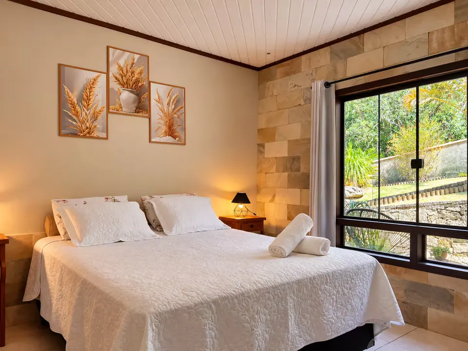 Suíte com cama de casal, parede de pedra e janela para o jardim